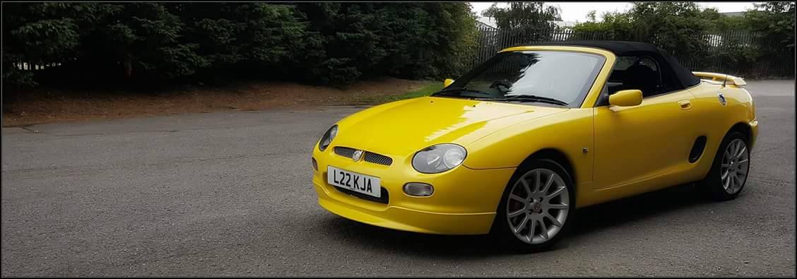 Yellow MGF convertible parked at an oblique angle on a forest road